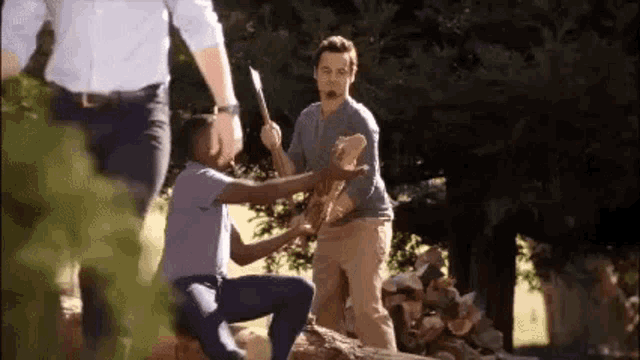 a group of men are standing around a pile of logs and one of them is holding a machete .