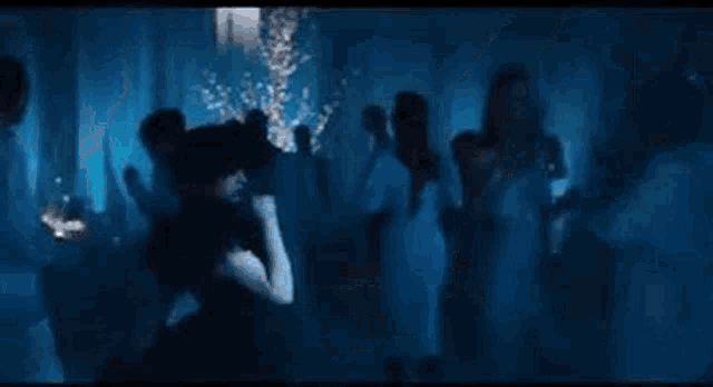 a woman in a black dress is standing in front of a crowd of people in a dark room .