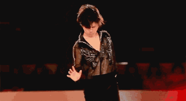 a young man in a black shirt is standing on a stage with his hand outstretched