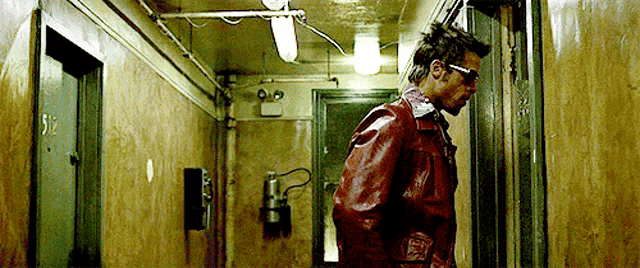 a man in a red leather jacket and sunglasses is walking down a hallway .