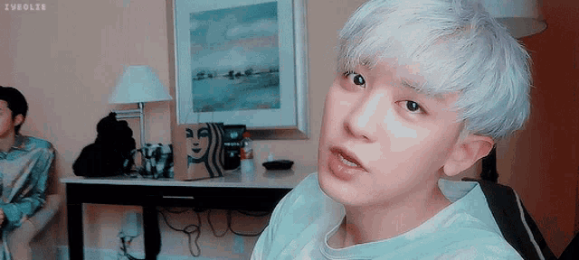 a young man with white hair is looking at the camera with a starbucks bag in the background