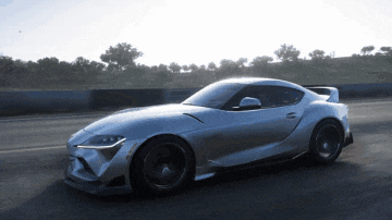 a silver sports car driving down a road with trees in the background