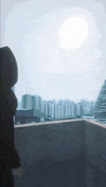 a person in a hoodie stands on a balcony overlooking the city