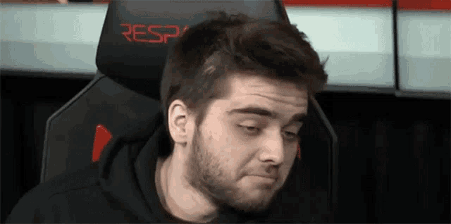 a man with a beard is sitting in a gaming chair and making a face .