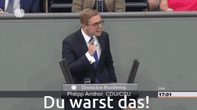 a man in a suit stands in front of a podium that says du warst das on it