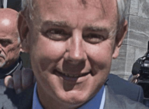 a man in a suit and blue shirt is smiling in front of a camera