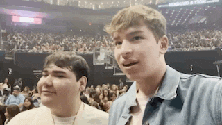 two young men are standing next to each other in front of a crowd of people at a concert .