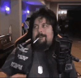 a man with a beard is sitting in front of a microphone smoking a cigarette .