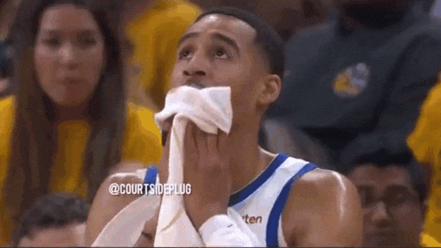 a basketball player is covering his mouth with a towel while watching a game .