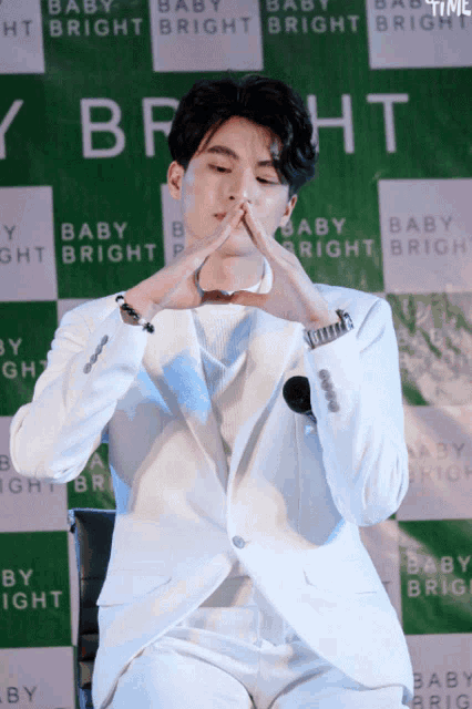 a man in a white suit is making a heart shape with his hands