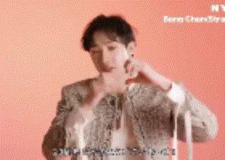 a man is standing in front of a pink background and making a heart shape with his hands .