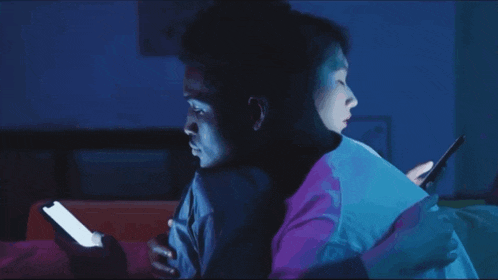 a man and a woman are looking at their phones at night