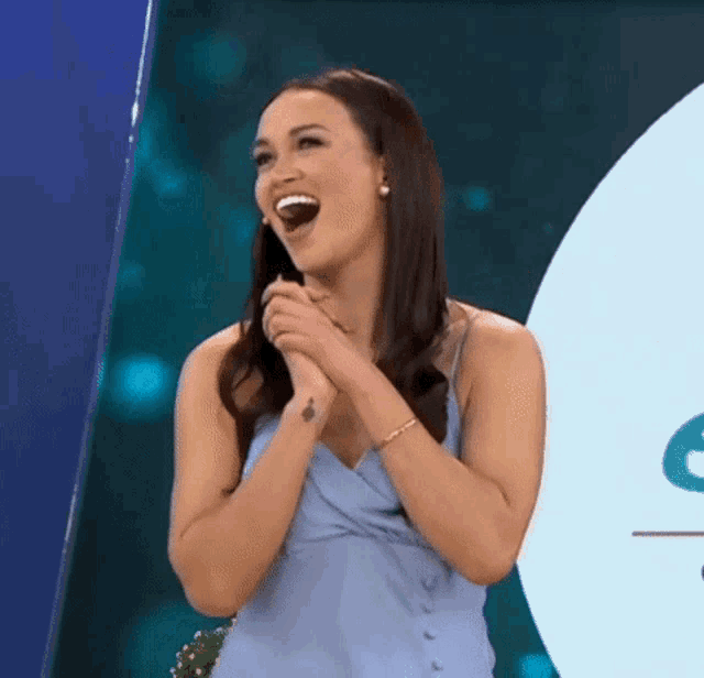 a woman in a blue dress is laughing and clapping her hands together .