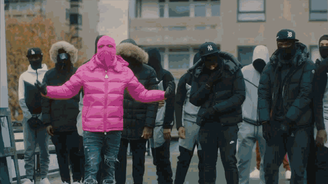 a man wearing a pink jacket and a ny hat stands in front of a group of people