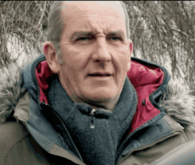 a man wearing a fur hooded jacket and scarf looks at the camera