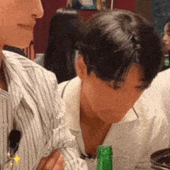 a man in a striped shirt is sitting at a table with a green bottle of beer .