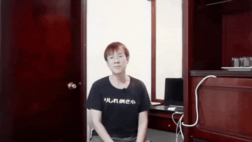 a man wearing a black shirt with chinese writing on it sits in a room