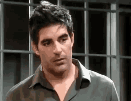 a man in a green shirt is standing in front of a window and making a funny face .