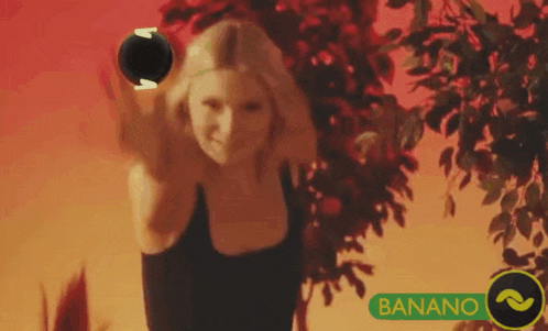 a woman in a black tank top is holding a black ball in her hand while standing in front of a tree .