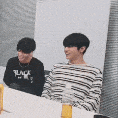 two young men are sitting at a table with bottles of liquid .