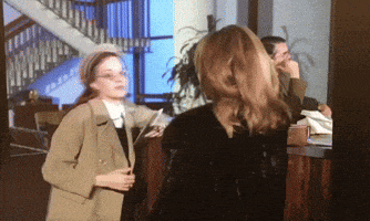 a woman in a trench coat stands next to another woman in a black dress