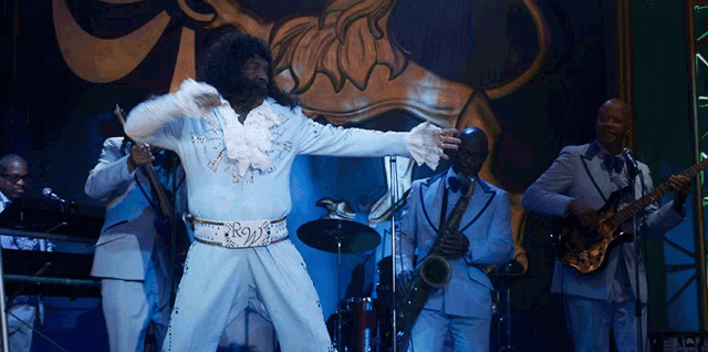 a man in a white suit is dancing on stage with a band
