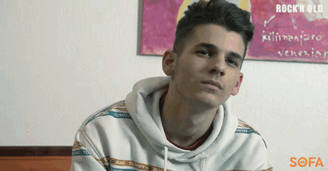 a young man wearing a tommy hilfiger sweatshirt looks at the camera