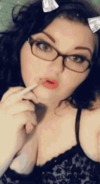 a woman wearing glasses and a cat ear headband is holding a cigarette in her mouth .