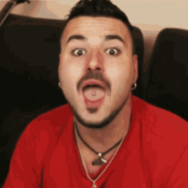 a man with a piercing in his tongue is wearing a red shirt and a necklace