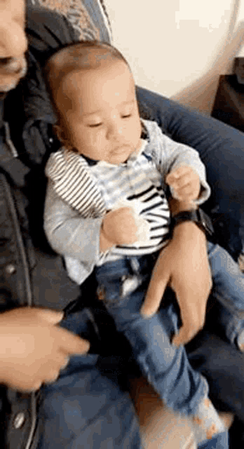 a man is holding a baby in his arms and the baby is looking at the camera .
