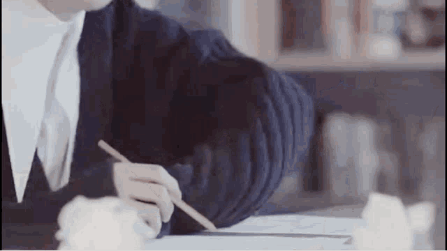 a person is sitting at a table writing with a pencil .
