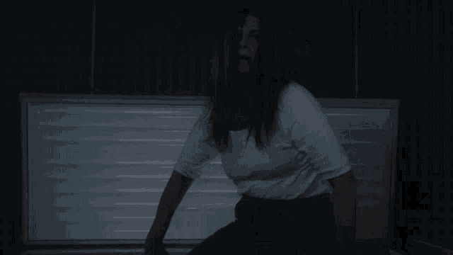 a woman in a white shirt and black pants is standing in a dark room