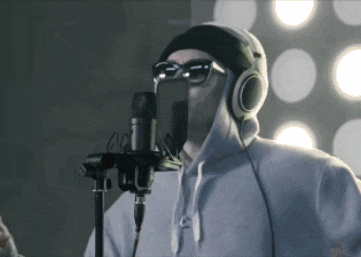 a man singing into a microphone wearing sunglasses and a beanie
