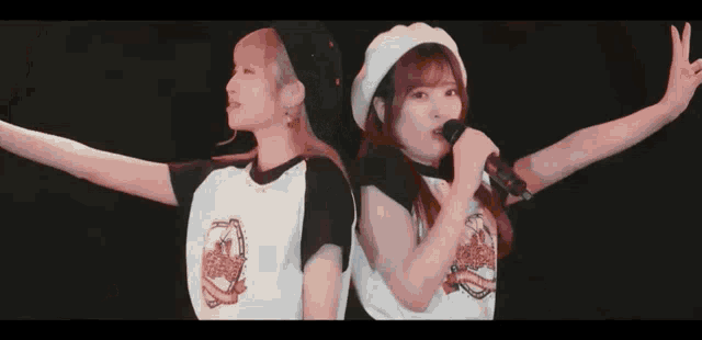 two girls are standing next to each other singing into microphones while wearing hats .