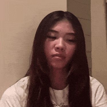 a woman with long brown hair is wearing a white t-shirt and a necklace .