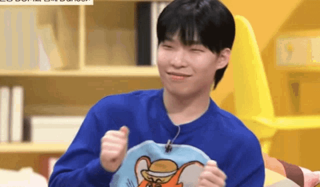 a young man in a blue sweater is holding a picture of a mouse .