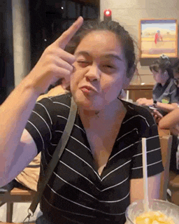 a woman is making a funny face while sitting at a table with a bowl of food .