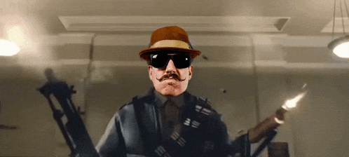 a man with a hat and sunglasses holds a gun