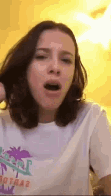 a woman is wearing a white t-shirt with a palm tree on it and making a funny face .