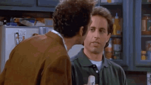 two men are standing next to each other in a room and one of them is holding another man 's hand in his mouth .