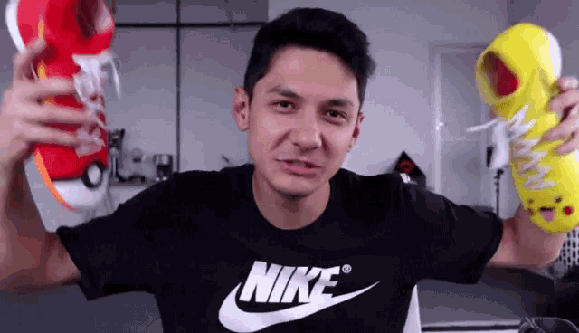 a man wearing a nike shirt is holding a pair of shoes
