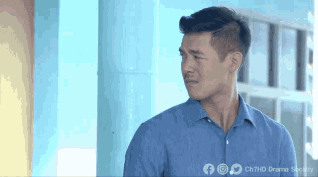 a man in a blue shirt is standing in front of a window with the words ch7hd drama society written on the bottom