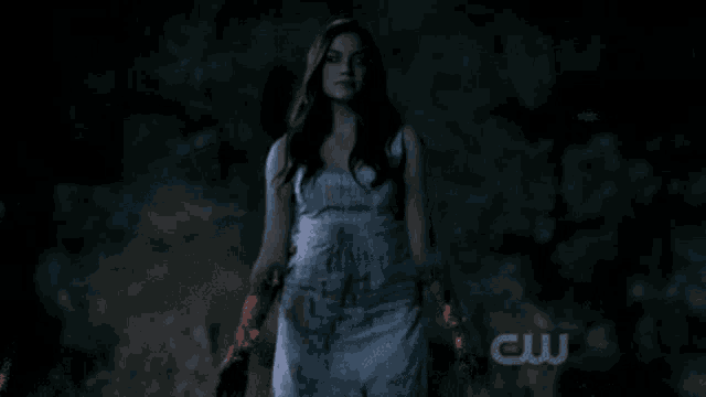 a woman in a white dress is standing in the dark with a cw logo in the corner .