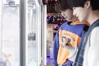 two young men are standing next to each other in front of a machine in an arcade .