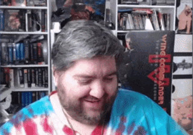 a man wearing a tie dye shirt is smiling in front of a book titled wing commander