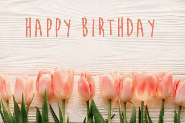 a happy birthday card with pink tulips on a wooden table