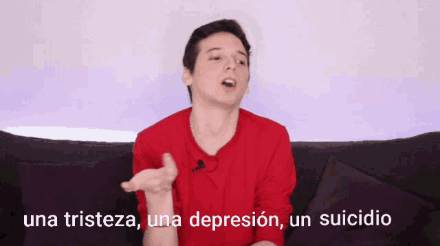 a man in a red shirt is sitting on a couch with the words una tristeza una depresion un suicidio behind him