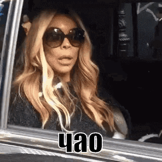 a woman wearing sunglasses is sitting in a car with her mouth open .