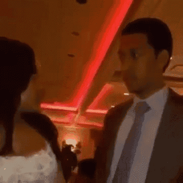 a man in a suit and tie is talking to a woman in a room with red lights .
