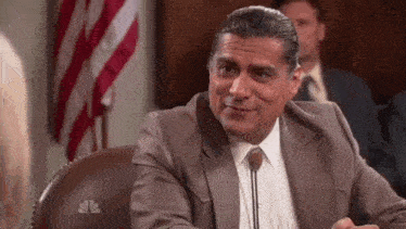 a man in a suit and tie is sitting at a desk in front of a microphone in a courtroom .